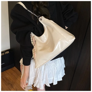 Close-up of beige patent leather crescent bag with metal chain strap and decorative scarf