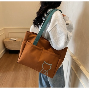 Detail view of canvas tote bag with deep green handles and cat embroidery in lifestyle setting