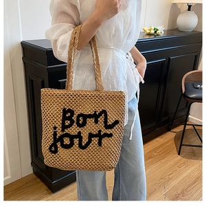 Détail du sac cabas en paille tissée avec lettrage Bonjour brodé en noir et anses