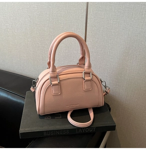 Détail du sac bowling rose en cuir grainé avec finitions argentées sur un livre