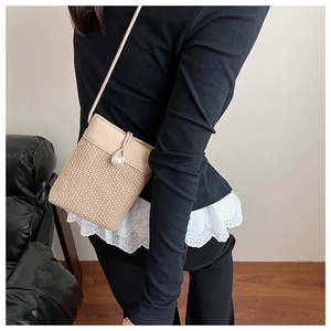 Detail of a beige woven crossbody bag featuring a large pearl clasp and thin strap
