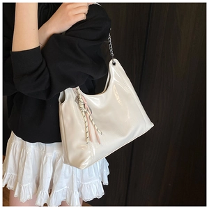 Close-up of cream patent leather tote with silver chain and braided rope charm detail