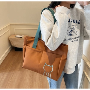 Detail of caramel canvas tote with green straps, cat embroidery and large front pockets