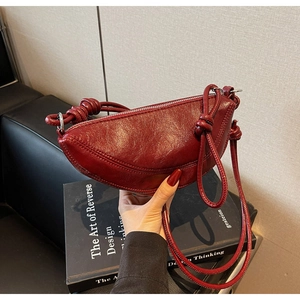 Dettaglio borsa a mezzaluna in pelle lucida bordeaux con tracolla a nodo elegante