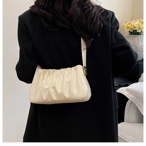 Detail of cream pleated cloud bag texture on shoulder with minimalist gold buckles
