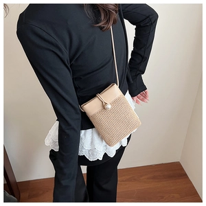 Detail of a mini woven straw crossbody bag featuring a pearl button and faux leather flap
