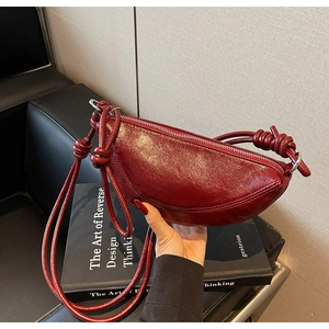Dettaglio borsa a mezzaluna in pelle bordeaux con tracolla annodata e cerniera liscia