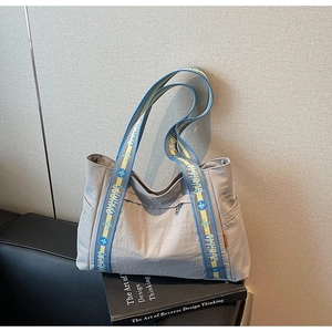 Detail of grey nylon tote bag with blue and yellow branded woven handles on a sofa
