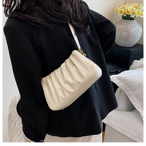 Detailed view of white pleated cloud bag in patent leather worn with black blazer