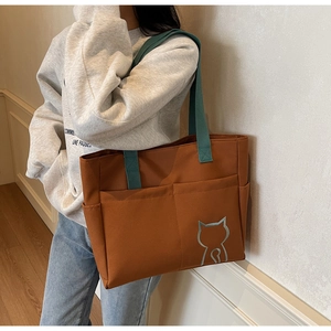 Detail of a brown tote bag with green straps and a blue cat embroidery for daily use