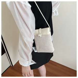Detail of woven straw crossbody bag featuring cream leather trim and a large pearl clasp