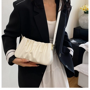 Detail of creamy white pleated cloud bag with shiny leather texture on model side