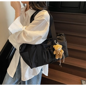 Detail view of large black canvas tote bag with drawstrings and a cute teddy bear pendant