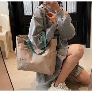 Detail of beige canvas tote bag featuring a blue cat embroidery and green handles
