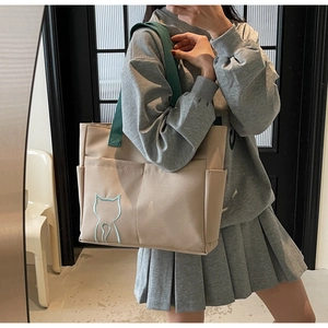 Close-up of beige canvas tote bag featuring a light blue cat embroidery and green strap