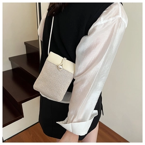 Detail of cream woven mini crossbody bag featuring an elegant pearl clasp and faux leather flap