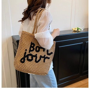 Détail du cabas en paille tressée avec broderie Bonjour noire porté par le mannequin