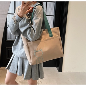 Detailed shot of beige canvas tote bag with green straps and cat embroidery shown on model