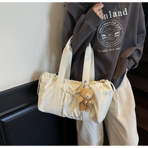 Detailed side view of cream drawstring canvas tote bag with brown teddy bear charm