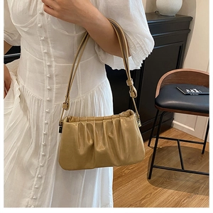 Close-up of khaki pleated cloud bag shoulder strap on model in white dress