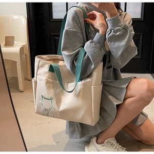 Detailed close-up of beige canvas tote bag with green straps and cat embroidery