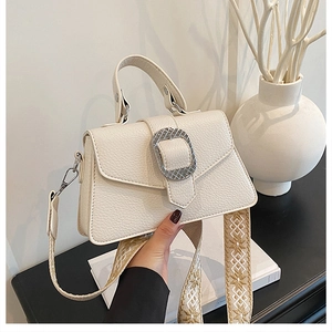 Detail einer weißen Handtasche aus Leder mit silberner Schnalle und Ethno-Schultergurt