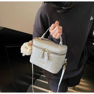 Détail d'un sac à main boîte gris clair avec poignée, bandoulière et pendentif en peluche