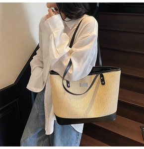 Close-up of woven straw tote bag with black leather trim and silver metal plaque