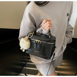 Détail du sac vanité noir avec logo doré, fermeture éclair et pendentif en peluche