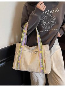 Large beige tote bag with colorful logo shoulder strap shown on a model in a casual setting