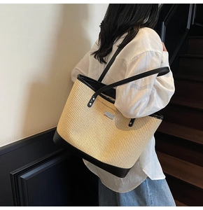 Detailed texture of large straw tote bag with black leather straps and silver metal logo
