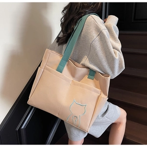Detail view of beige canvas tote with green strap and cat embroidery on wooden stairs