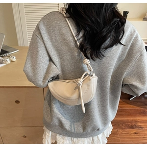 Dettaglio della borsa a mezzaluna beige con tracolla annodata e zip argentata