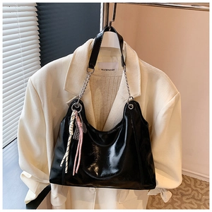 Detail of glossy black tote bag with silver chain strap and pink tassel accessory