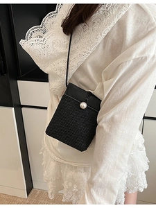 Women's woven straw crossbody bag with black leather trim and large pearl buckle closure
