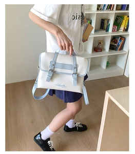 Detail of college style cream and blue crossbody bag with metal buckles and leather straps
