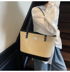 Detail of a large straw tote bag with black leather trim and small metal logo plaque
