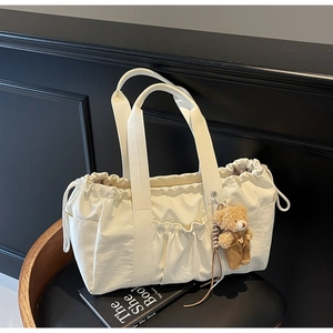Detail of cream canvas tote featuring drawstring closure and cute plush bear charm