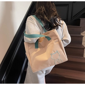 Side view of large beige canvas tote bag with green straps and cat embroidery