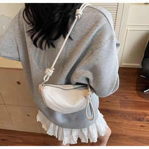 Dettaglio di una borsa a mezzaluna bianco crema con tracolla decorata da nodi indossata