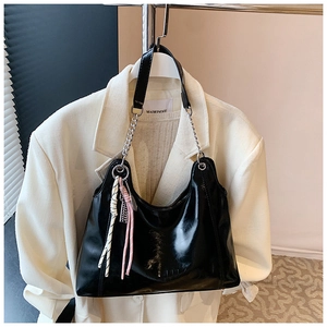 Detail of glossy black patent leather tote bag with silver chain strap and tassels