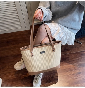 Macro view of woven straw tote bag with brown leather handles and a metallic logo detail