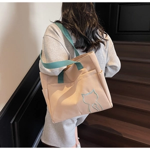 Close-up of canvas tote bag with green cat embroidery and functional side pockets