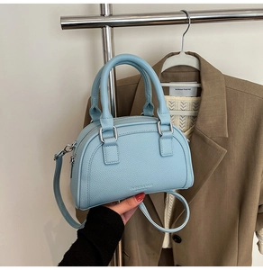 Détail d'un sac bowling en cuir bleu clair tenu devant un blazer de couleur beige