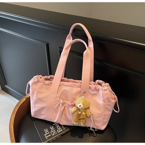 Pink drawstring nylon tote bag with pocket and a cute plush bear charm on a chair