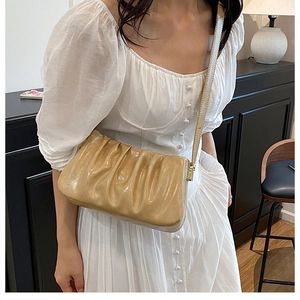 Detail of a beige ruched cloud bag with thin strap and gold metal hardware on model