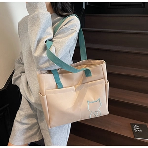 Detail of beige canvas tote with blue cat embroidery and functional side pockets