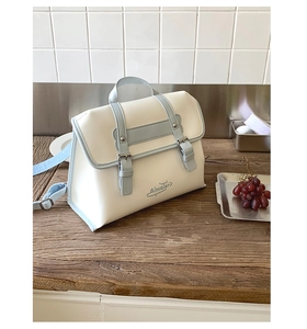 Detail view of stylish tote bag with cream PU leather and blue trim on wooden table