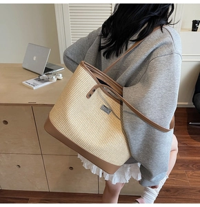 Detail of woven straw tote bag featuring brown leather trim and metallic brand plaque