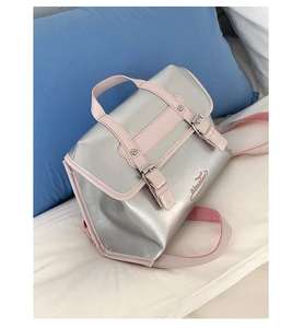 Detail of silver metallic backpack with pink trim and buckle straps on a soft blue pillow